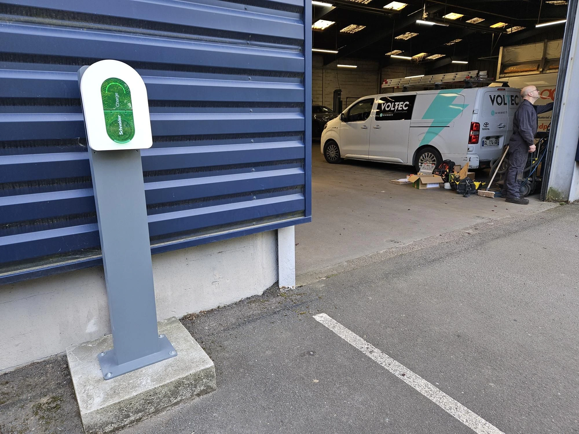 Borne de recharge Schneider Electric Charge installée, vue d'ensemble avec véhicule Voltec en arrière-plan