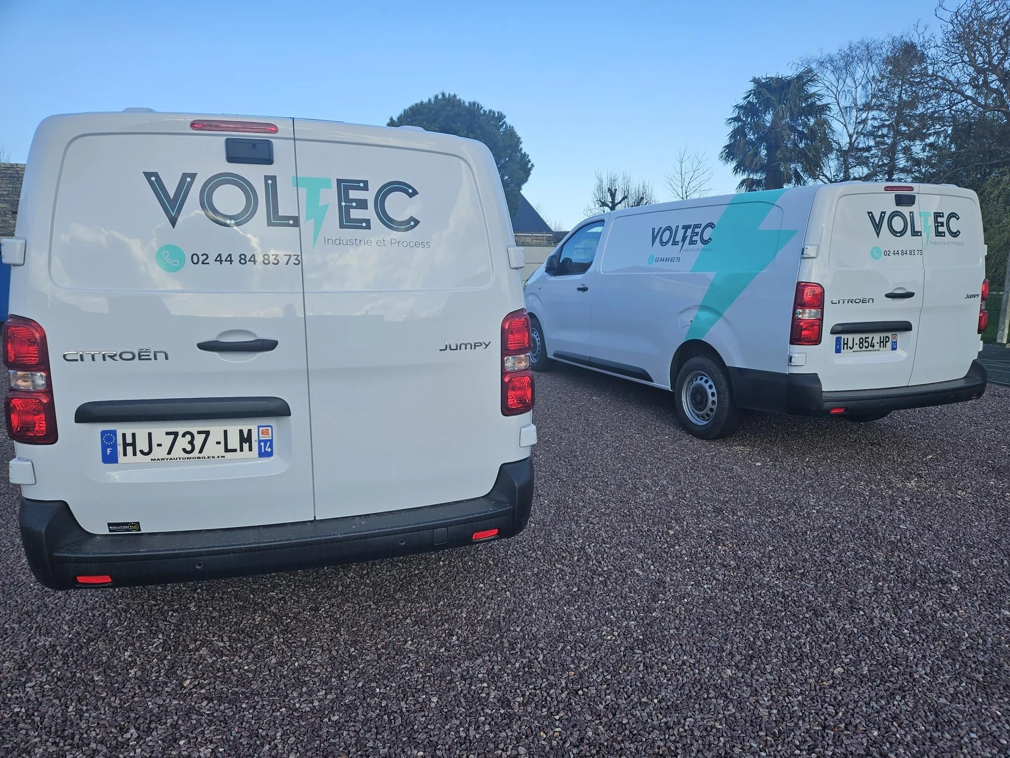 Véhicules Voltec Industrie et Process stationnés dans une cour, avec un troisième véhicule en arrière-plan
